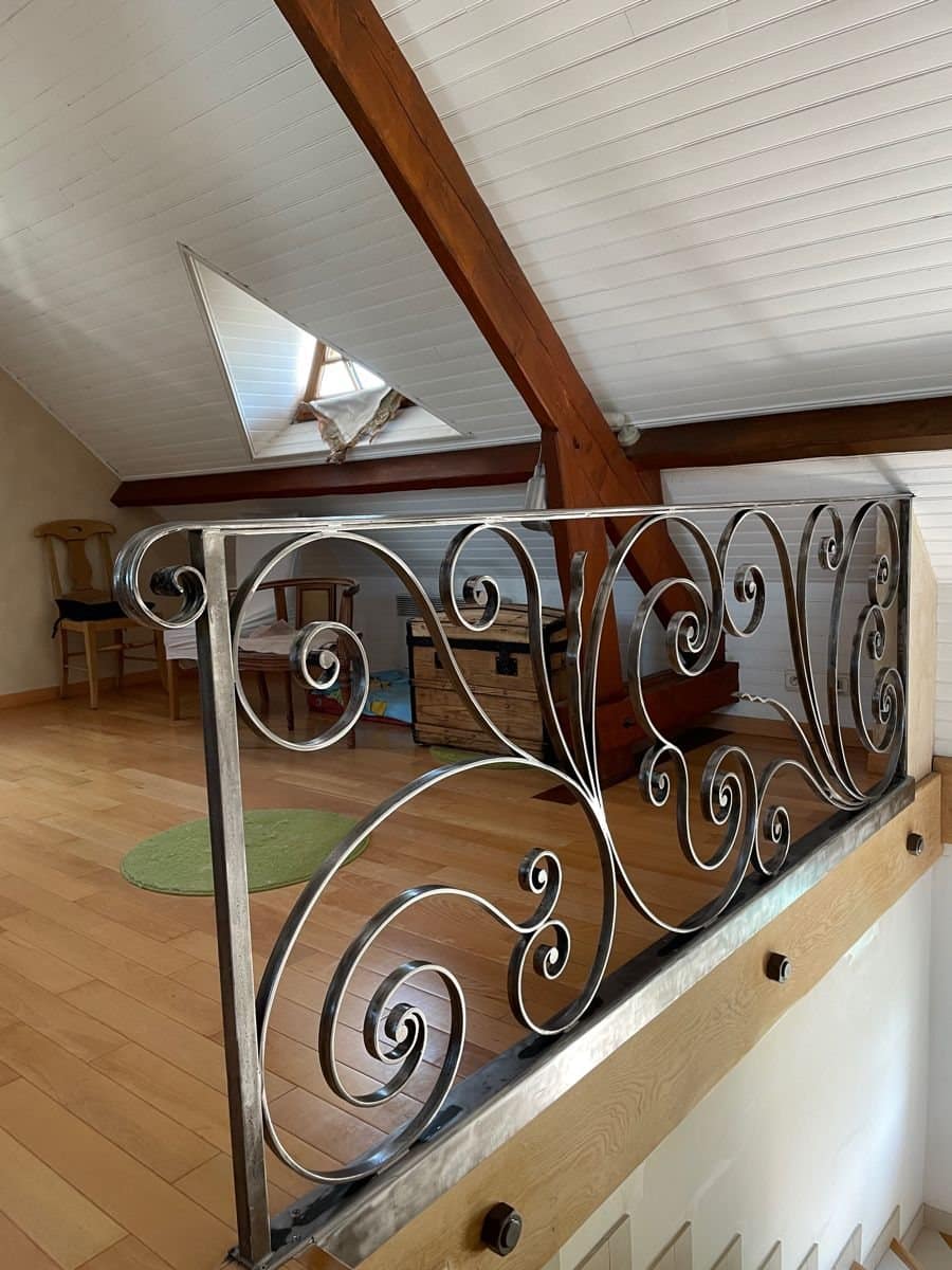 Borstwering in ruw staal met grote krullen aan de rand van een mezzanine onder een zichtbaar dakgebinte