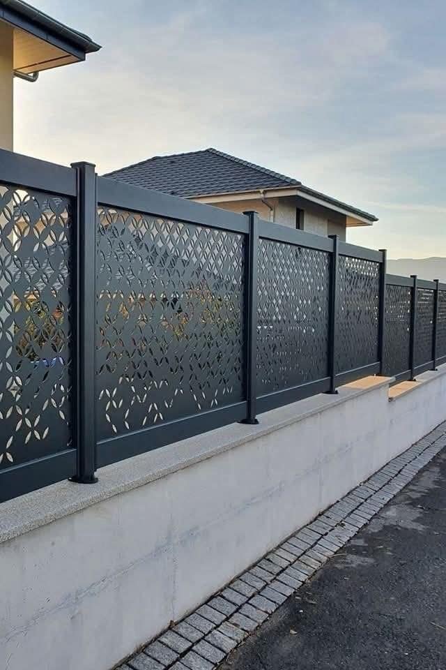 Zwarte stalen omheining met uitgesneden decoratieve panelen, op een betonnen muurtje langs een nieuwbouwwoning
