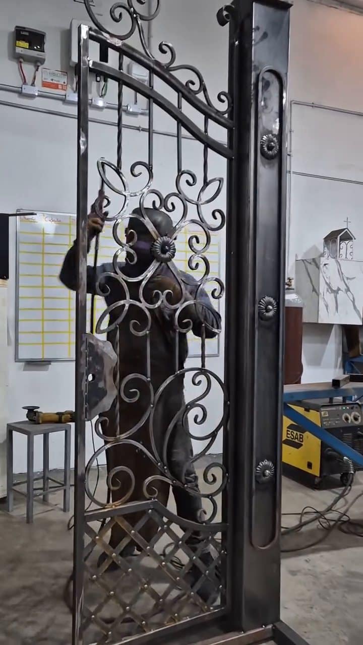 Lasser aan het werk achter een smeedijzeren poortje met krullen, op de palen gemonteerd in het atelier