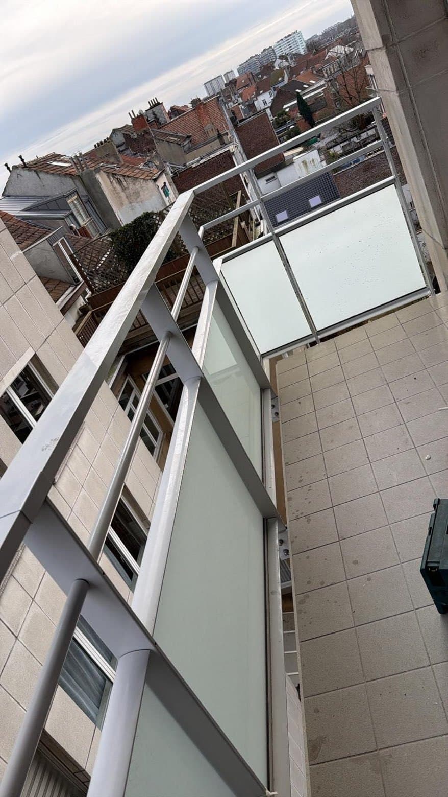 Balkonborstwering met wit kader en vulling in mat glas, op een verdieping boven de daken van de stad