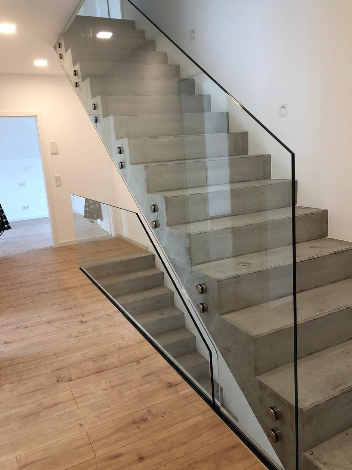 Straight staircase with a frameless glass balustrade, side-fixed with steel clamps, in a newly built house